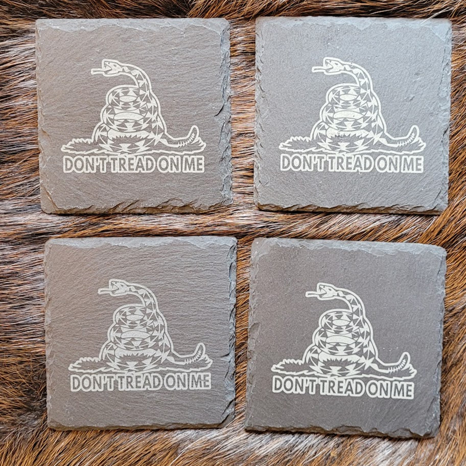 Four natural slate coasters laser engraved with the Gadsden Flag Don't Tread on Me snake design, sitting on a fur pelt.